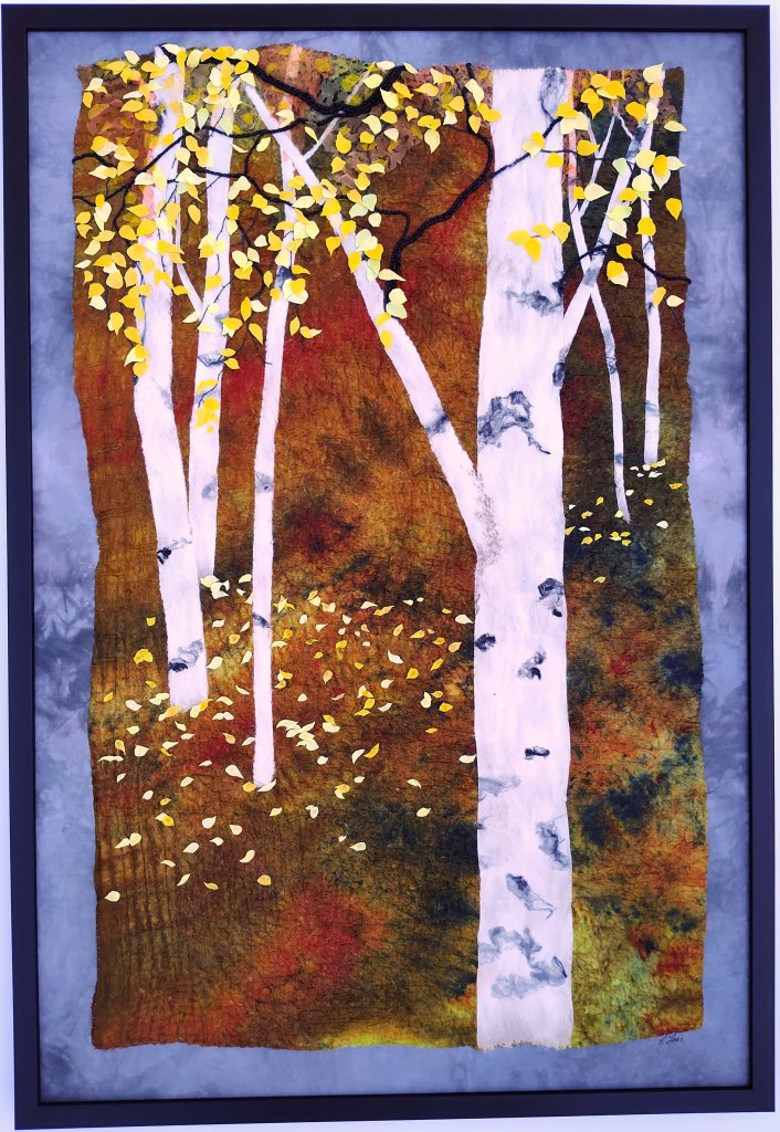 Textile artwork of autumn landscape with birch trees and fallen leaves.