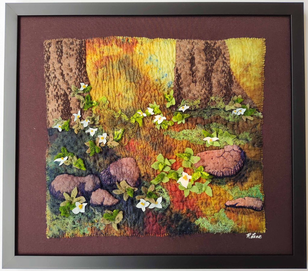 Textile artwork with sunlight streaming between two tree trunks on to the rocks and flowers in the foreground.