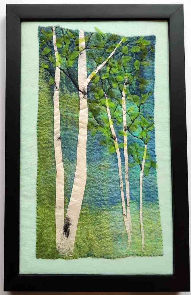 Framed textile artwork with spring birch trees on green and blue background.